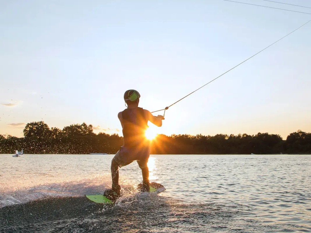 Wakeboarder silhouetted against the sunset at a cable park, being pulled by the line as the board sprays water